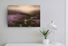 A landscape painting depicting a misty valley with purple heather, dark rocky terrain, and small waterfalls under a soft sky, above a plant and lamp.